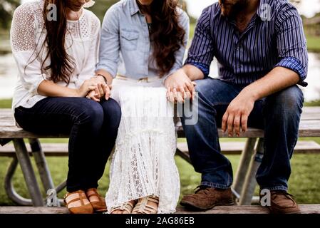 Closeup shot of people sitting on the bench while holding hands and a blurred background Stock Photo
