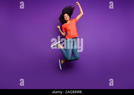 Full length body size photo of cheerful charming nice pretty sweet girlfriend jumping up rejoicing in victorious glory wearing jeans denim orange t Stock Photo