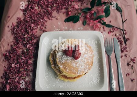 High angle shot of a delicious pancake with berries and pink flower petals on the ground Stock Photo