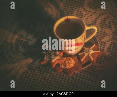 Espresso cup decorated with Santa Claus paintings on plate with home made gingerbread. Delicious sookies and aromatic coffee on table in candle light Stock Photo