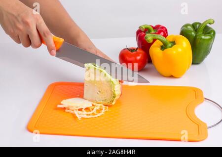 housewife cutting cabbage with knife on plastic cutting board on white background Stock Photo