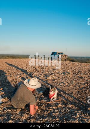 Vertical shot of a person controlling the drone using his phone sitting next to a cute dog Stock Photo