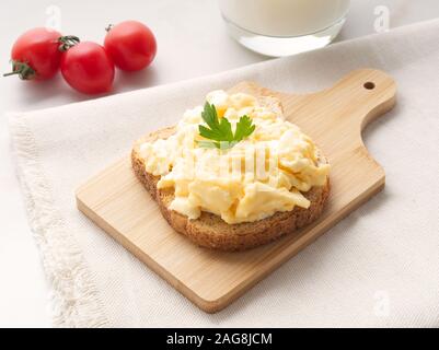 Sandwich with pan-fried scrambled eggs on a wooden cutting board, side view. Stock Photo