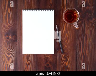 The open notepad with spiral , pencil, cup of tea on a dark brown wooden table, top view Stock Photo