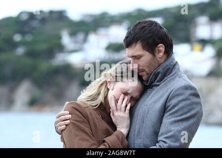 Worried man comforting a sad woman in winter on the beach Stock Photo