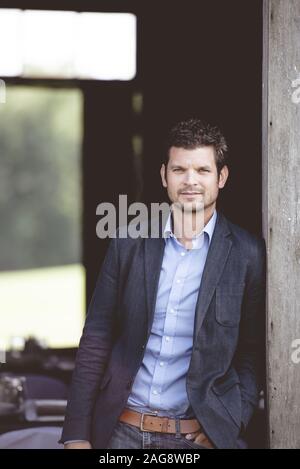 Vertical shot of a well-dressed male leaning against the wall and looking at the camera Stock Photo
