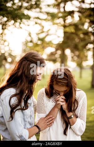 Vertical shot of two female with their eyes closed and praying with a blurred background Stock Photo