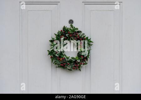 A Christmas Holly wreath hanging from a white wooden front door Stock Photo