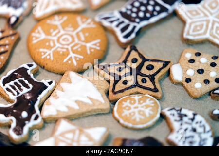 Many different shapes and drawings of homemade Christmas gingerbread on paper. The cookies are decorated with white glaze and chocolate. Close up view Stock Photo