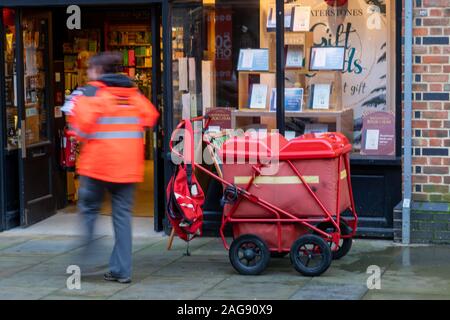 A Postman or postwoman delivering mail using a cart or trolley, the post person is blurred to show movement Stock Photo