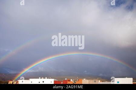 rainbow in the sky against cloud, row of flat-roofed houses at the front, Aguimes in Gran Canaria Stock Photo