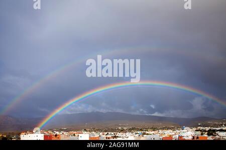 rainbow in the sky against cloud, row of flat-roofed houses at the front, Aguimes in Gran Canaria Stock Photo