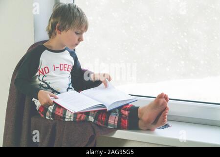 Child reads book by the window. Beautiful winter weather with snow falling Stock Photo