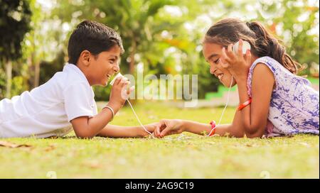 Two children having fun by playing with String Telephone at park during vacation - Concept of brain development and socializing by playing outdoor Stock Photo