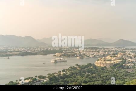 Elevated view of lake Pichola flanked by City Palace, Lake Palace, and Aravalli hills at sunrise in summer in Udaipur, Rajasthan, India. Stock Photo