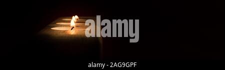Three burning candles in wooden candle holder with copy space against dark background Stock Photo