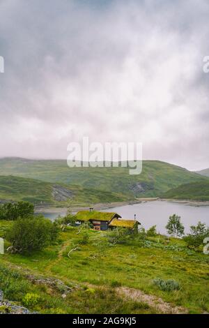 Norwegian wooden summer house overlooking scenic lake, Norway, Scandinavia. Cottage By Lake In Rural. Peat roofed hut on Lake. Typical grass roofed Stock Photo