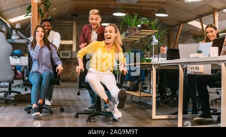 Office fun. Joyful coworkers enjoying office chair race Stock Photo