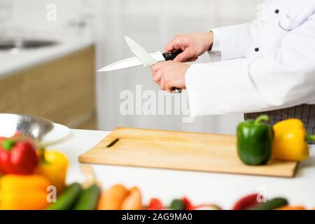 Unrecognizable Chef Man Sharpening Knives Working In Kitchen Indoor, Cropped Stock Photo