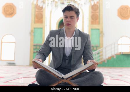 Religious young hafiz muslim man praying inside the mosque and reading holy book of qoran or koran. Stock Photo