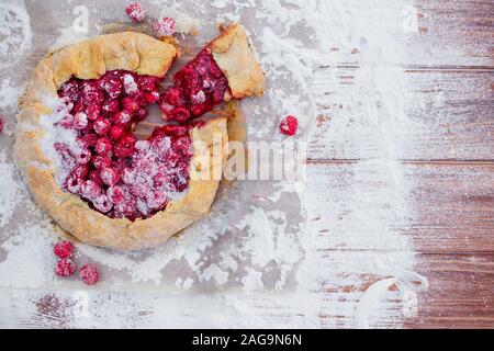 Homemade fruit pie galette made with fresh raspberries with powdered sugar on wooden table. Open pie, raspberry tart. Summer berry dessert. Flat lay. Stock Photo