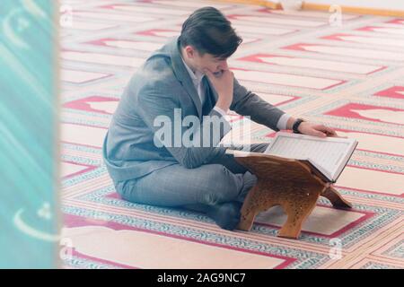 Religious young hafiz muslim man praying inside the mosque and reading holy book of qoran or koran. Stock Photo