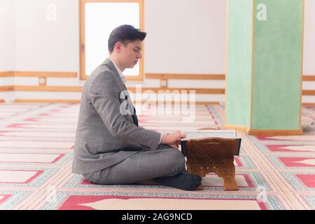 Religious young hafiz muslim man praying inside the mosque and reading holy book of qoran or koran. Stock Photo