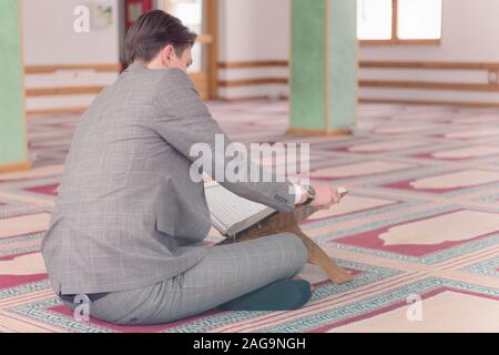 Religious young hafiz muslim man praying inside the mosque and reading holy book of qoran or koran. Stock Photo