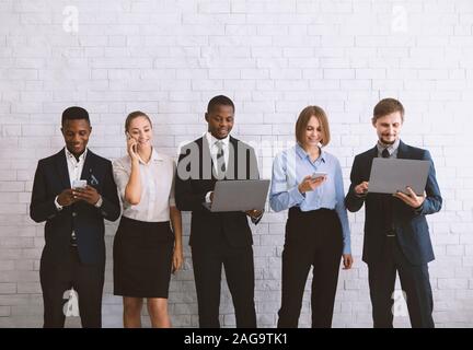 Young diverse team using modern gadgets, near white brick wal Stock Photo