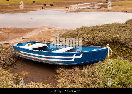 An old blue and white wooden aground boat on the mud while low tide. Stock Photo