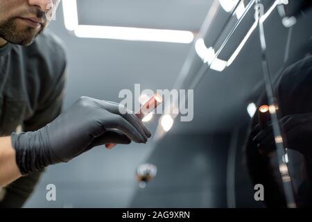 Worker examining vehicle body for scratches and damages backliting by a flashlight at the service. Checking car paint before vehicle detailing Stock Photo