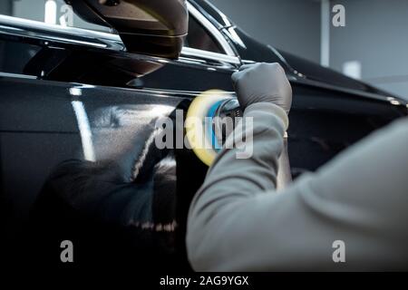Car service worker polishing vehicle body with special wax from scratches, close-up. Professional car detailing and maintenance concept Stock Photo