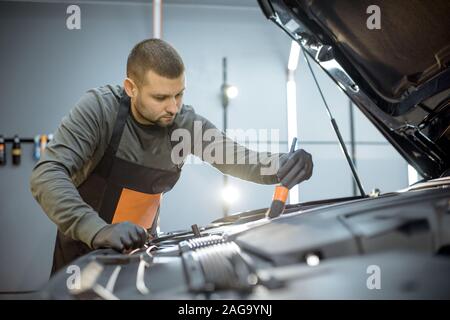 Man performs a professional car cleaning, washing engine with brush and detergent at the service station Stock Photo