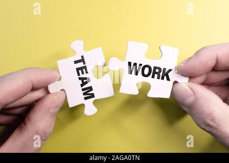 teamwork concept with hand connecting puzzle pieces against yellow background Stock Photo