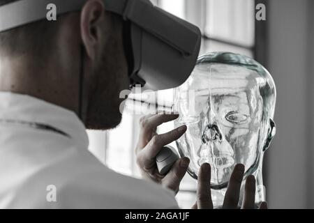 A young doctor wearing VR goggles examining a mannequin in VR simulation - future technology concept Stock Photo