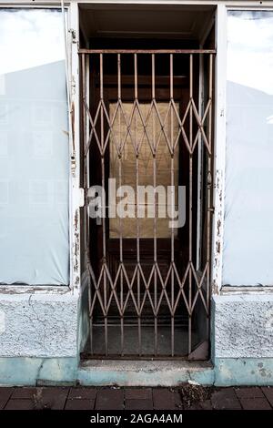 Door of an abandoned shop secured with a steel grille, the windows sealed with paper and foil Stock Photo