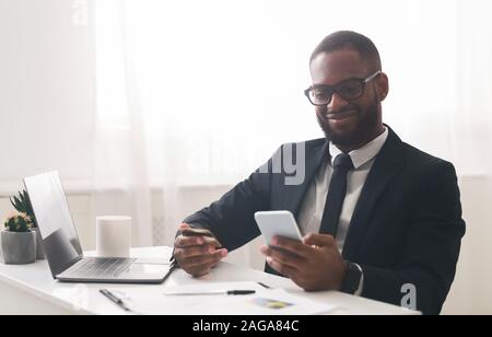 Cheerful guy in glasses holding credit card, making purchases online Stock Photo