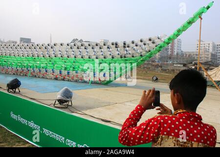 Dhaka, Bangladesh. 18th Dec, 2019. A boy takes a photo of a boat made out of empty plastic bottles at the exhibition.BD Clean members collected 3 million empty plastic bottles from various parts of Bangladesh as a homage to the three million martyrs who sacrificed their lives in the Liberation War of 1971. Artistes crafted various objects, including a mural of Bangabandhu, boats and the map of Bangladesh, using the scraps. The works were put on display at Mohakhali's T&T Colony playground in Dhaka on the eve of Victory Day. Credit: SOPA Images Limited/Alamy Live News Stock Photo