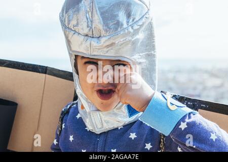 portrait of a funny little child girl disguised as a superhero fighting the bad guys with homemade costume, cardboard plane wings and astronaut helmet Stock Photo