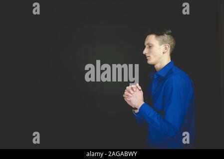 Male praying while his eyes are closed with a black background Stock Photo
