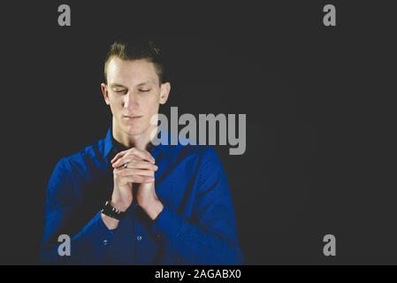 Male praying while his eyes are closed with a black background Stock Photo