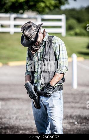Vertical shot of a male wearing a cowboy out if with his hands on the belt and looking down Stock Photo