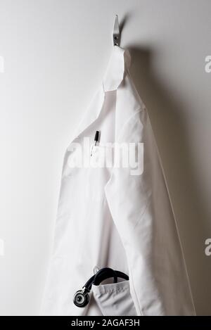 A Doctors White Lab Coat and Hanging on a Hook with Stethoscope in pocket. Stock Photo