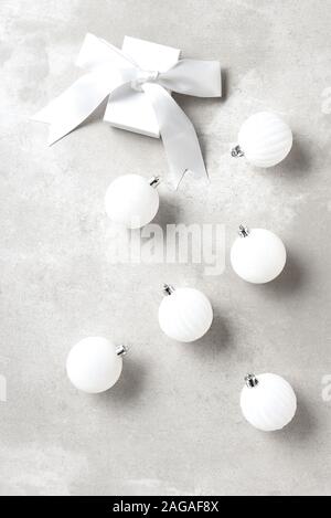 White Christmas Tree Ornaments on a light gray table top with a white gift box and bow. Stock Photo