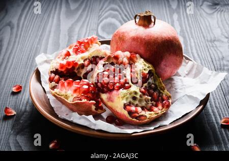 close-up, ripe pomegranates on a brown ceramic bowl on a black wooden table Stock Photo