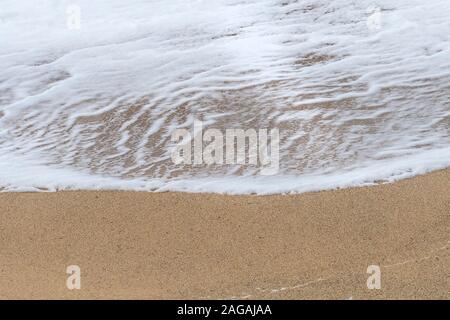 The foam of a small wave left behind on a beach as the wave recedes. Stock Photo