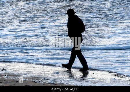 The silhouette of a man walking along the shoreline on Fistral Beach in evening light in Newquay in Cornwall.
