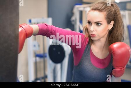 Female boxer hitting a huge punching bag. Woman boxer training actively and hard. Self defence and anti violence training Stock Photo