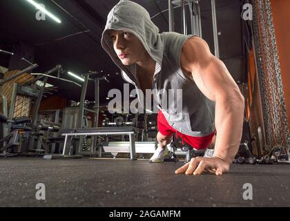 Young sporty man doing push ups exercise with one hand in fitness gym. Healty lifestyle concept Stock Photo