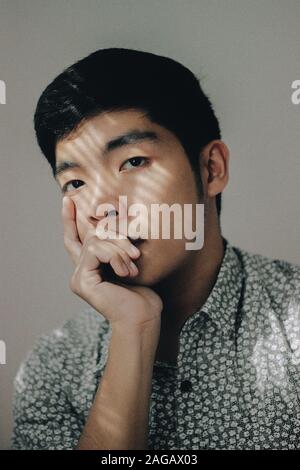 Vertical shot of Asian male thinking with his hand under the chin on white background Stock Photo
